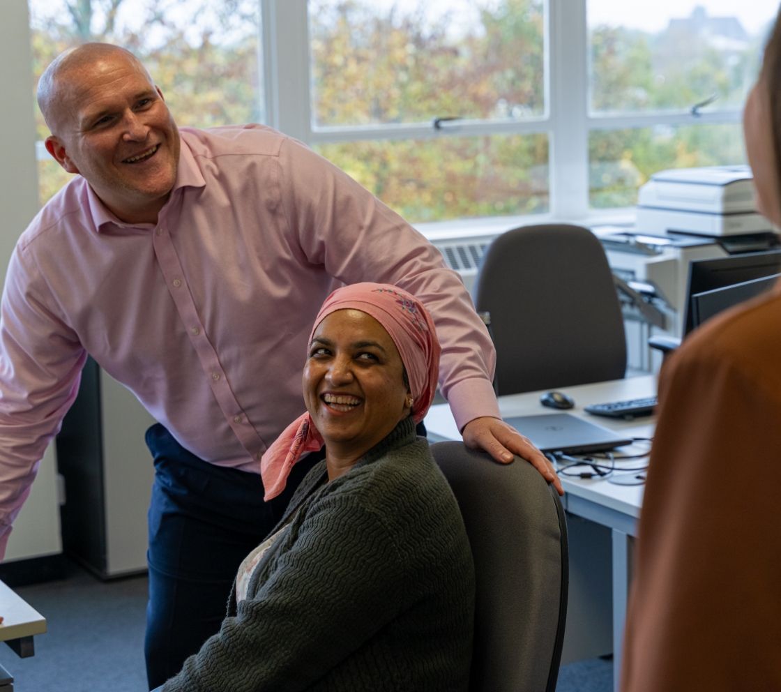 People surrounding a desk in an office talking and smiling