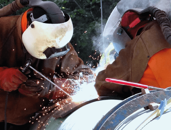 Construction worker wearing a face shield welding pipes