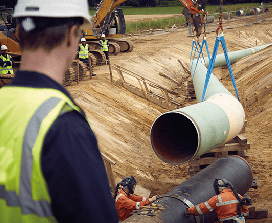 construction worker overlooking a construction site where pipes are being lifted