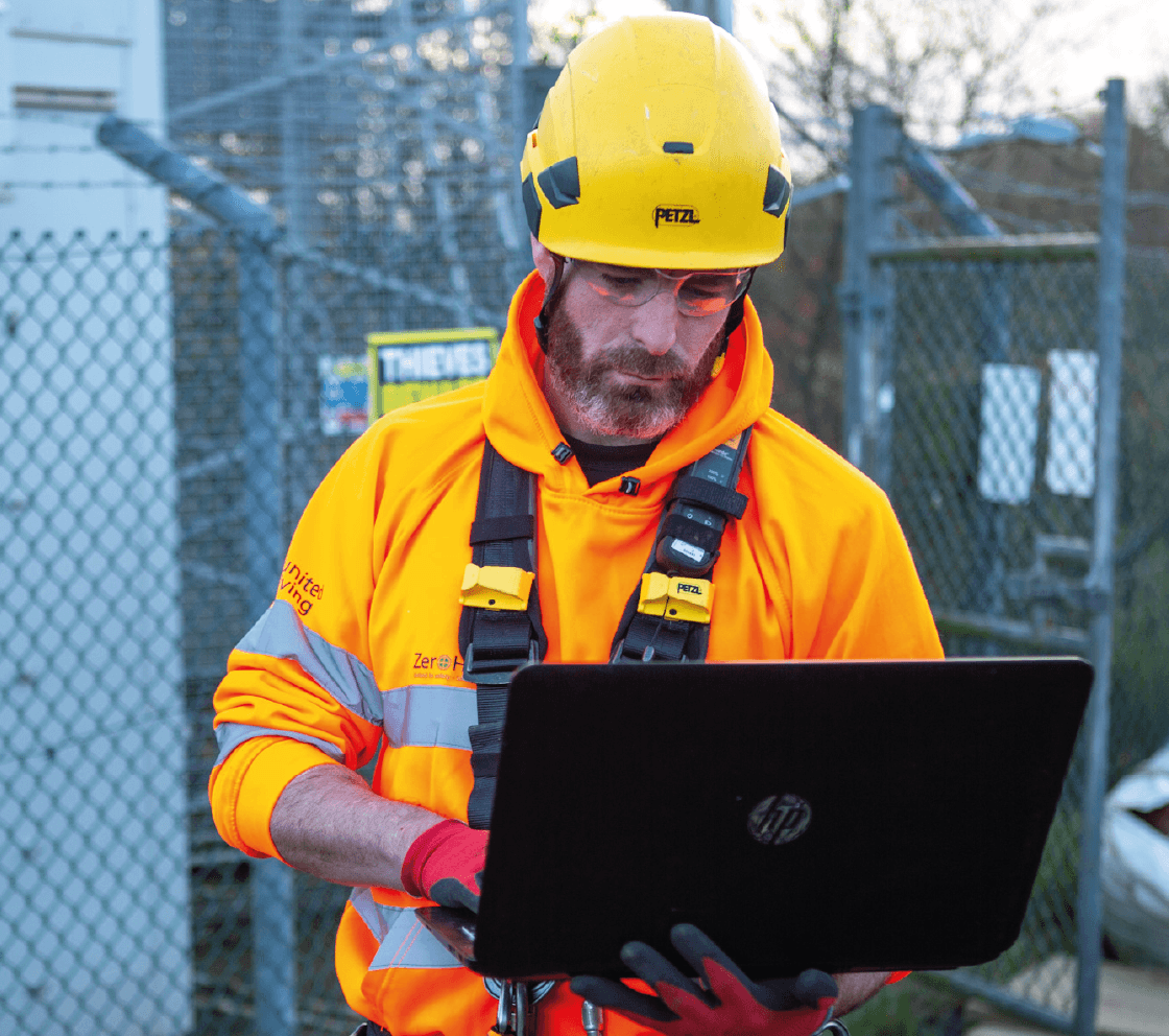 engineer working on laptop in front of telecom tower