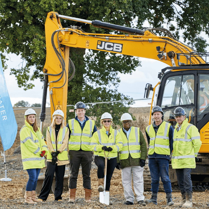 Group of United Living employees standing on site in front of a digger and holding a spade
